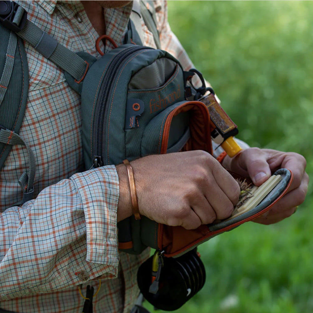 Shown is the Fishpond Canyon Creek Check Pack with an angler selecting a fly from the front compartment drying patch