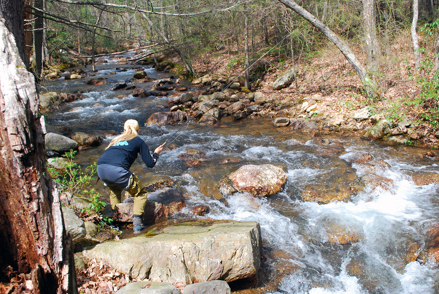 Brook trout guided fishing trip - fly fishing angler standing in a rocky stream on a sunny day holding a fly rod and fishing for brook trout