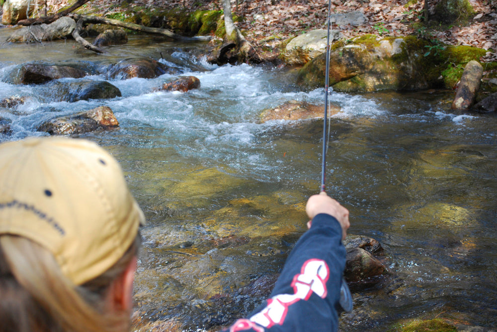 Fly fishing on a small mountain stream with clear water surrounded by a rocky bottom and angler is casting into a small pool