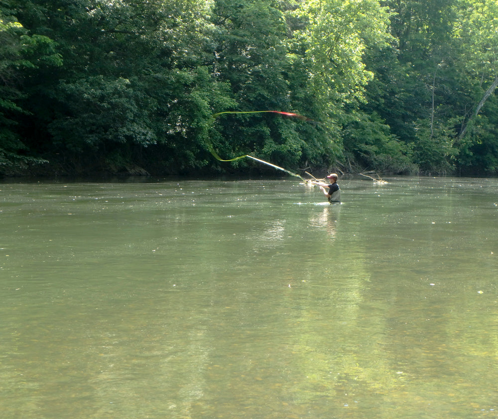 Fly fishing angler standing in a river casting fly rod.