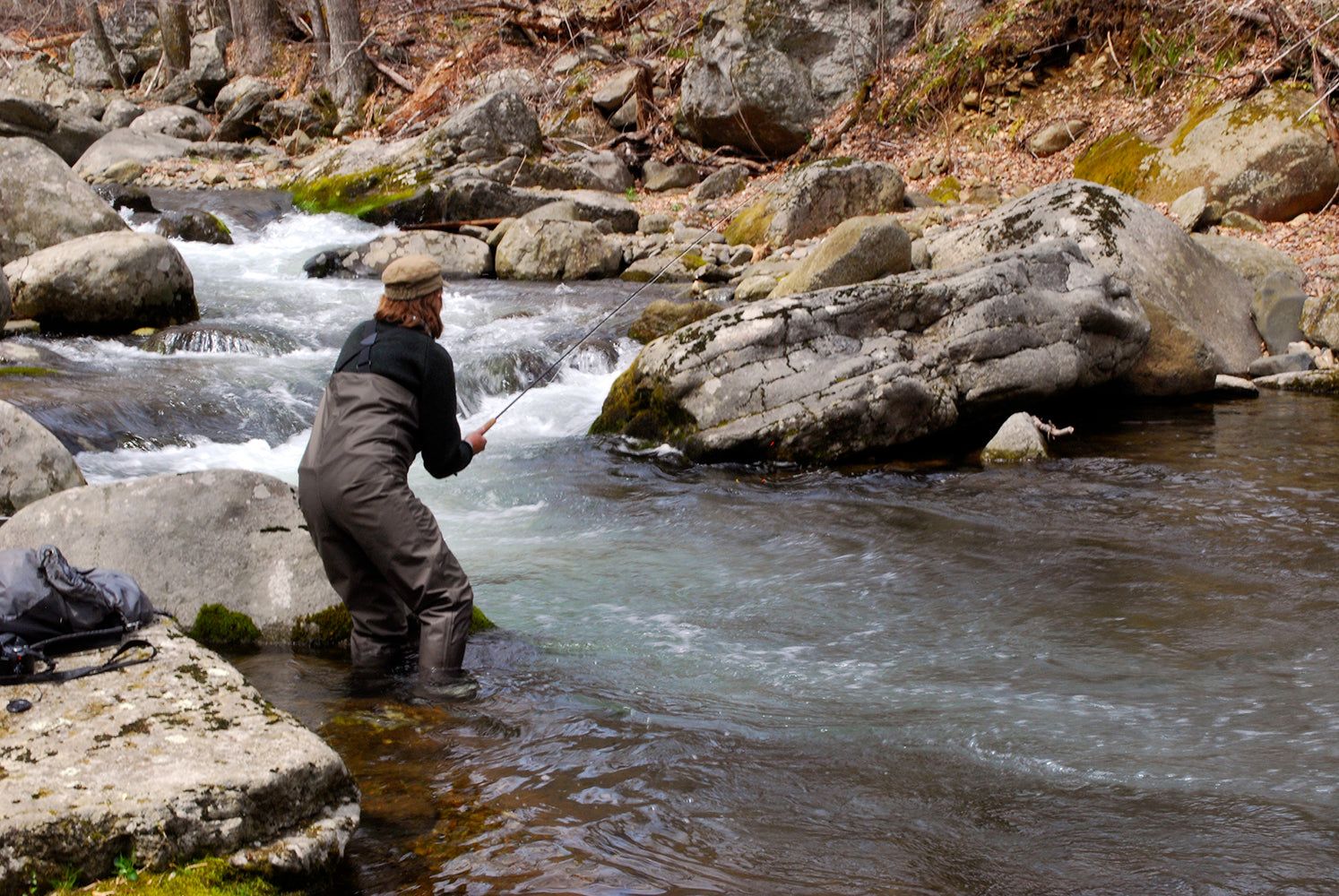 Virginia native brook trout stream with boulders and a clear water and small waterfalls and an angler fly fishing while standing in the water